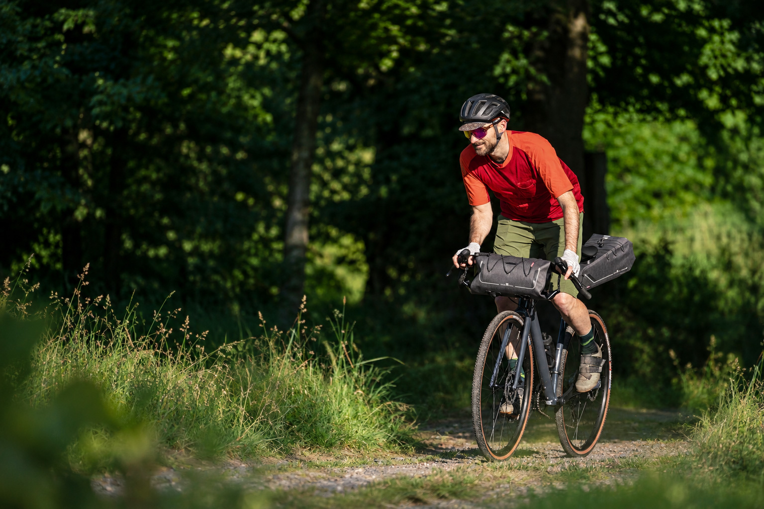Cyclist riding a woodland trail with grey handlebar and saddle bags