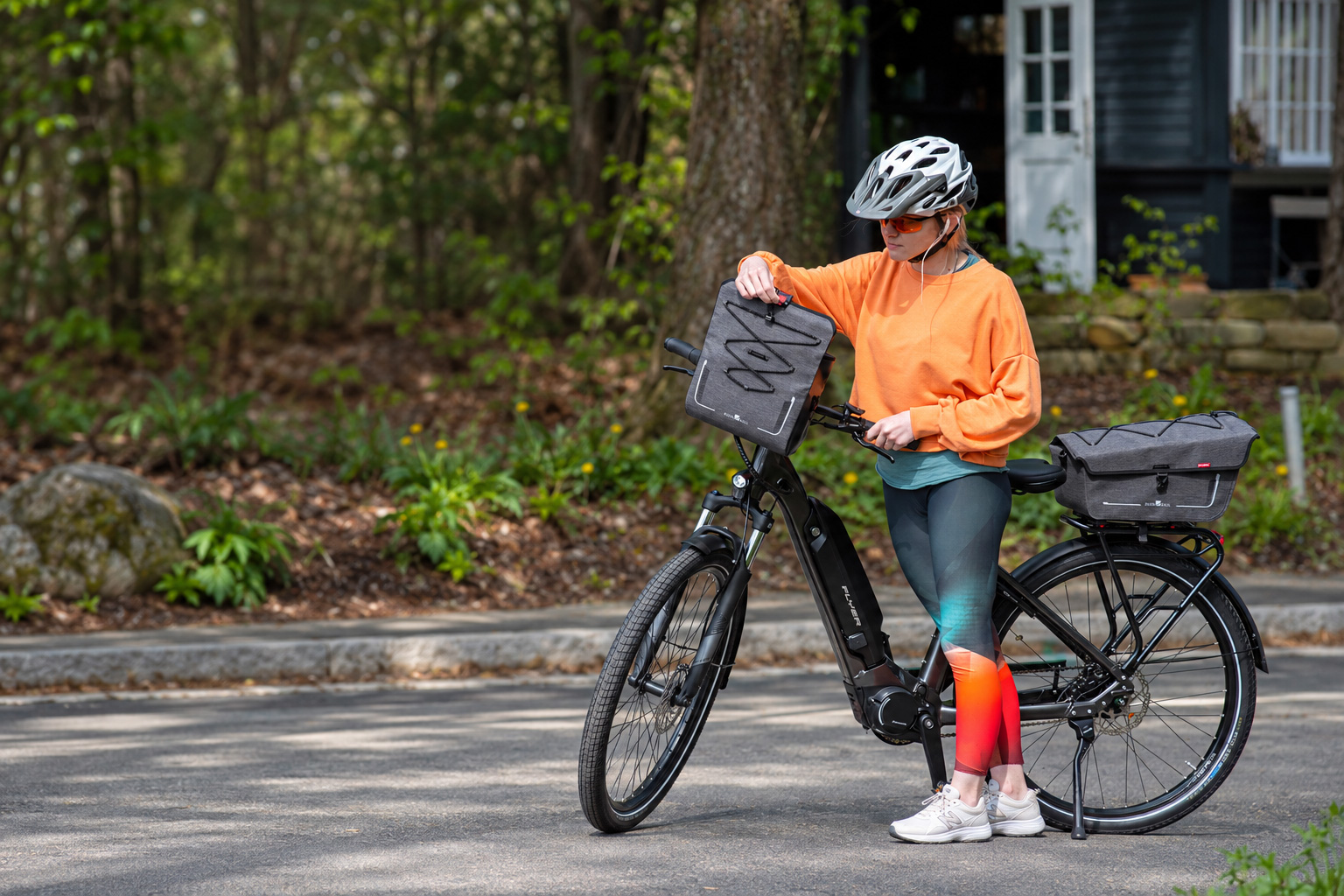 Cyclist in an orange sweatshirt with grey bags on a black bicycle